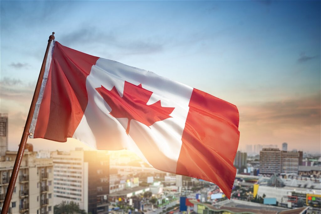 Canadian flag waving above a cityscape at sunset