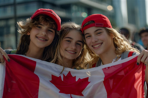 Three people smiling and holding a Canadian flag, wearing red caps, with an urban background.